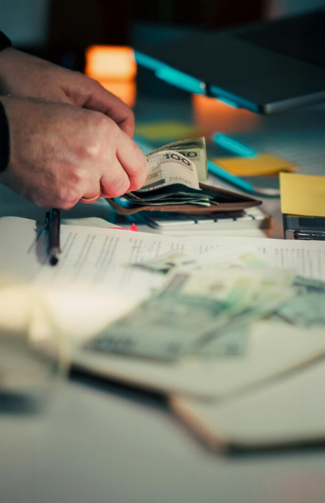 Close-up of hands counting cash next to a wallet and documents on a desk.
