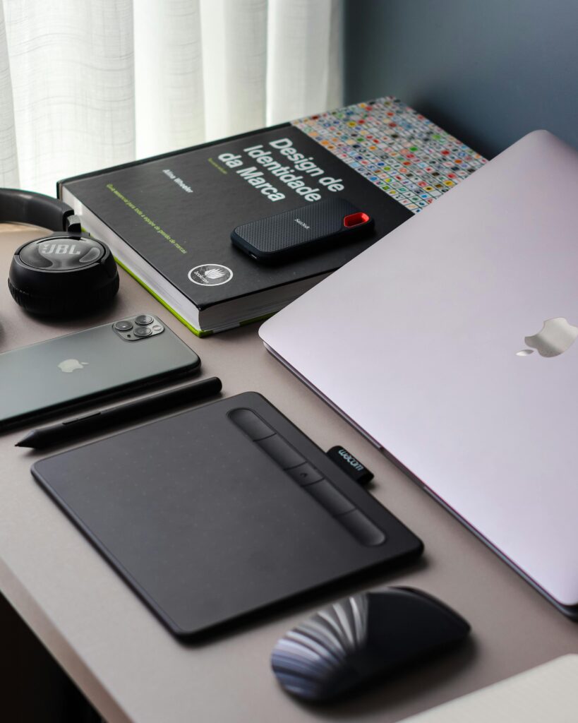 A neatly arranged desk setup featuring a laptop, smartphone, headphones, and drawing tablet.