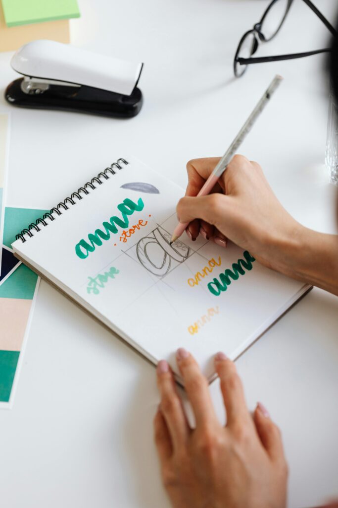 Close-up of creative handwriting practice in a spiral notebook on a designer's desk.