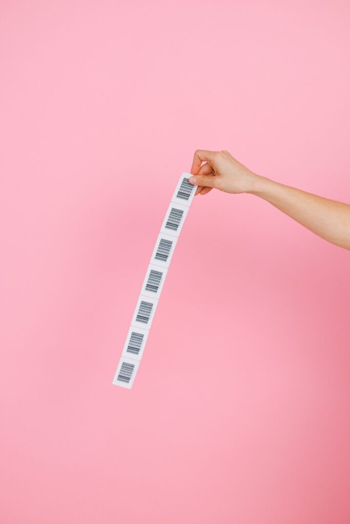 A hand holds a strip of barcodes against a pink background, creating a simple yet striking image.
